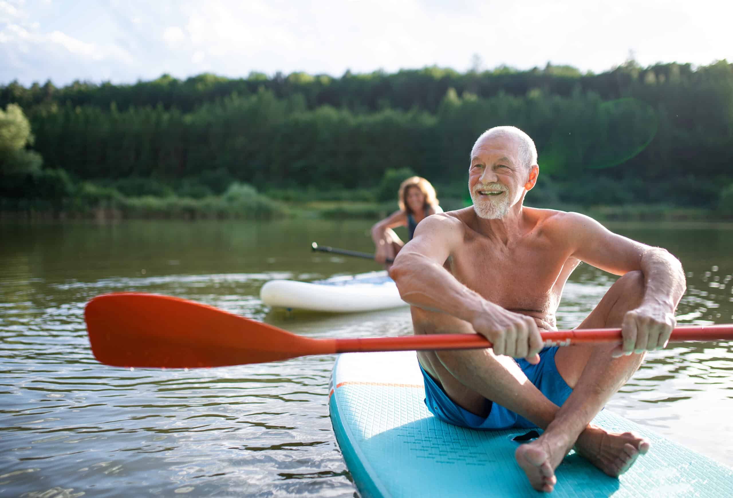 senior couple paddleboarding on lake in summer.